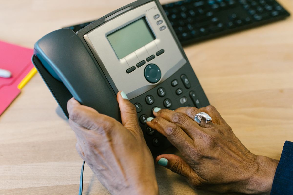 Hands dialing an office desk phone, representing a dental office's call-handling system