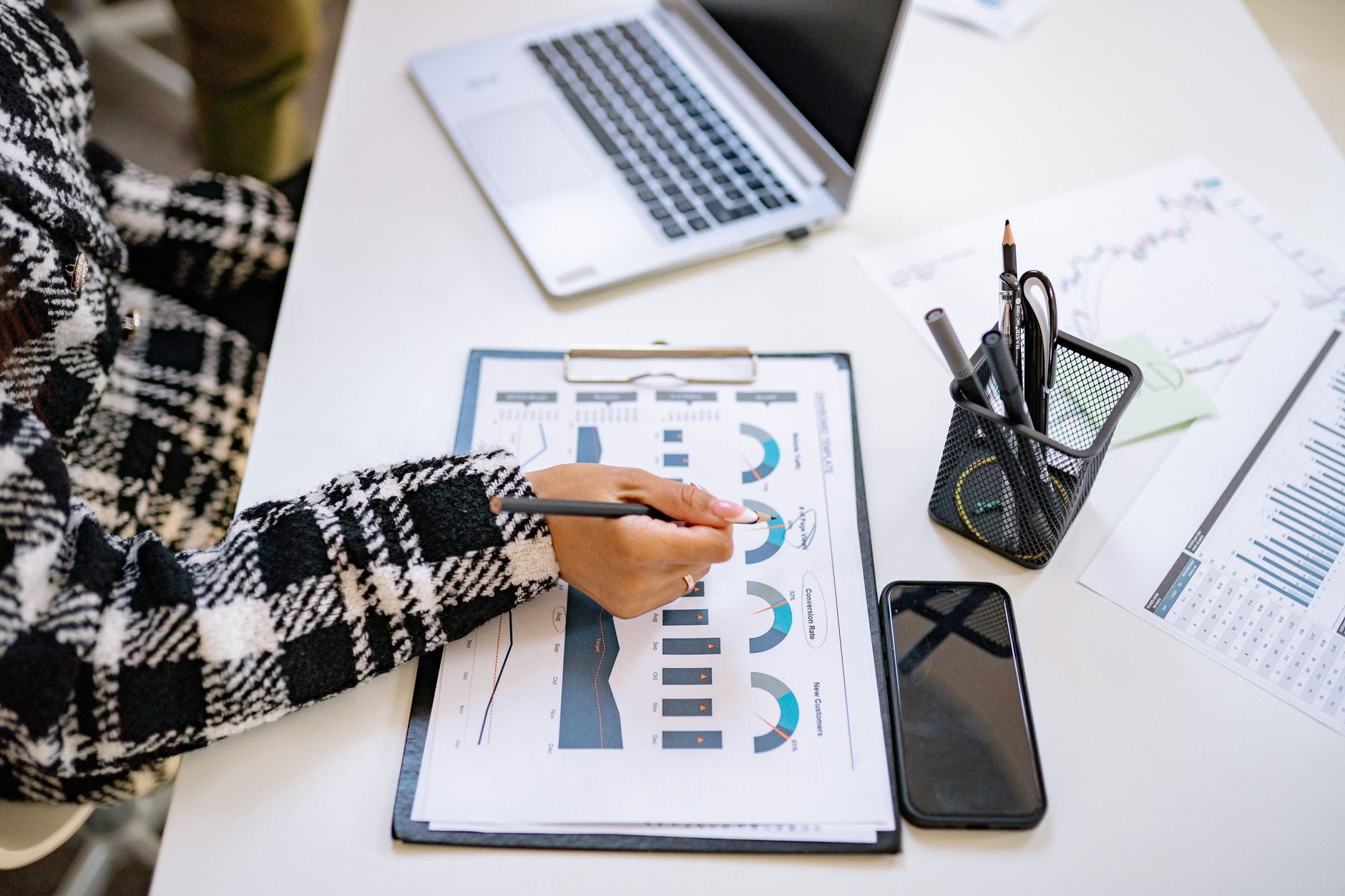 Person reviewing conversion and new-customer charts on a clipboard beside a laptop